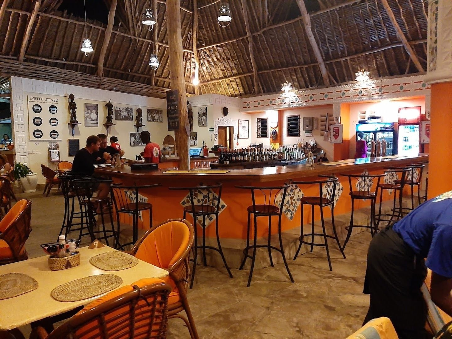 Jolly's thatched-roof bar at night, lanterns glowing over the orange-painted counter and stools