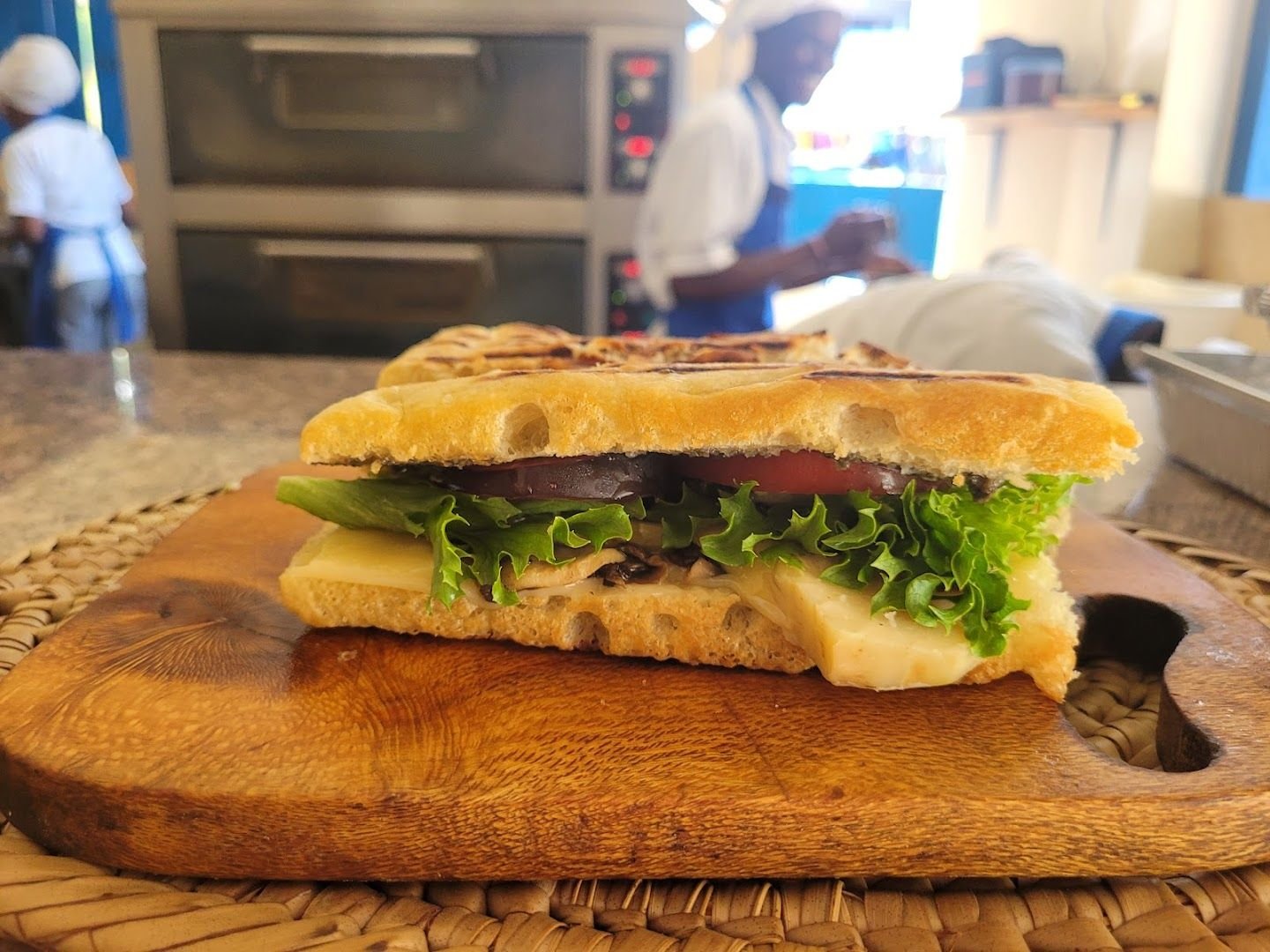 A grilled panino sliced open, melted cheese and vegetables, the kitchen at work behind