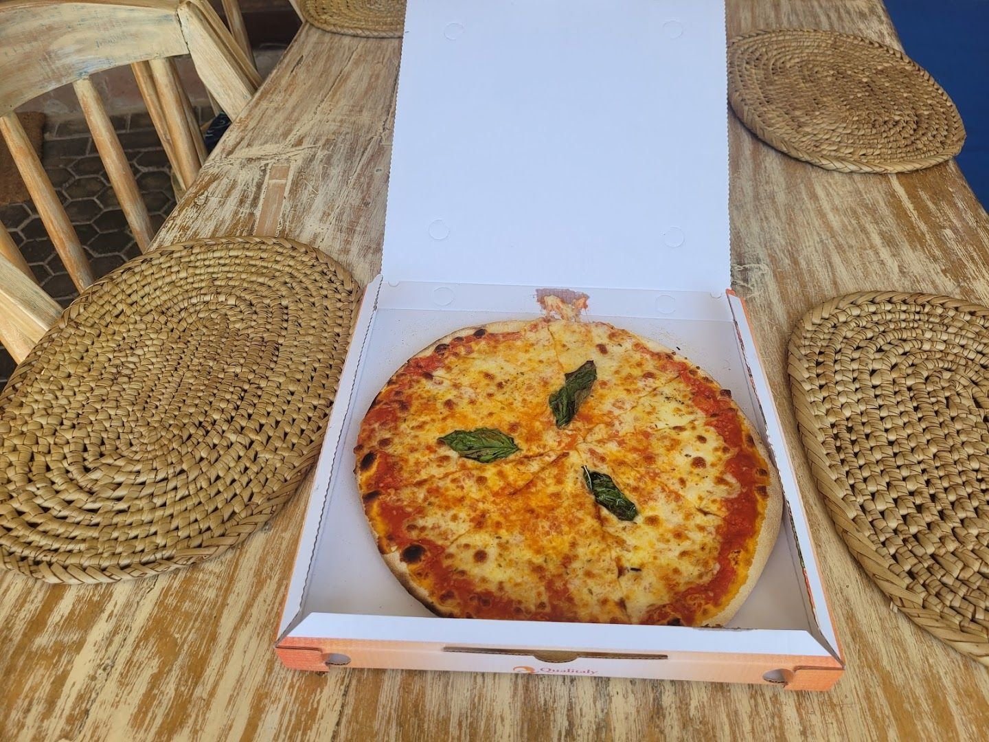 A sliced Margherita pizza, fresh from Jolly's oven, on a rustic outdoor table